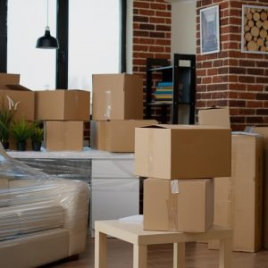Nobody in empty living room with cardboard packaging at new home, furniture things in stack of carton boxes. No people in household property with package cargo to move in, real estate.
